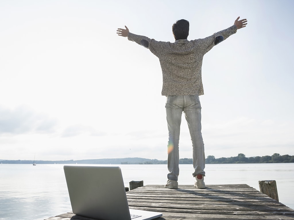 Mann mit Notebook auf Steg am See