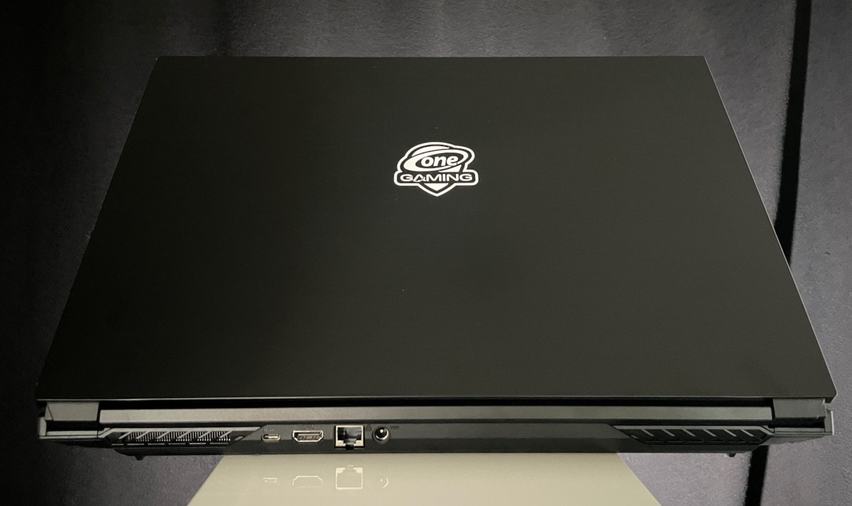 Schwarzer Laptop von hinten leicht aufgeklappt auf weißem Podest vor schwarzem Vorhang