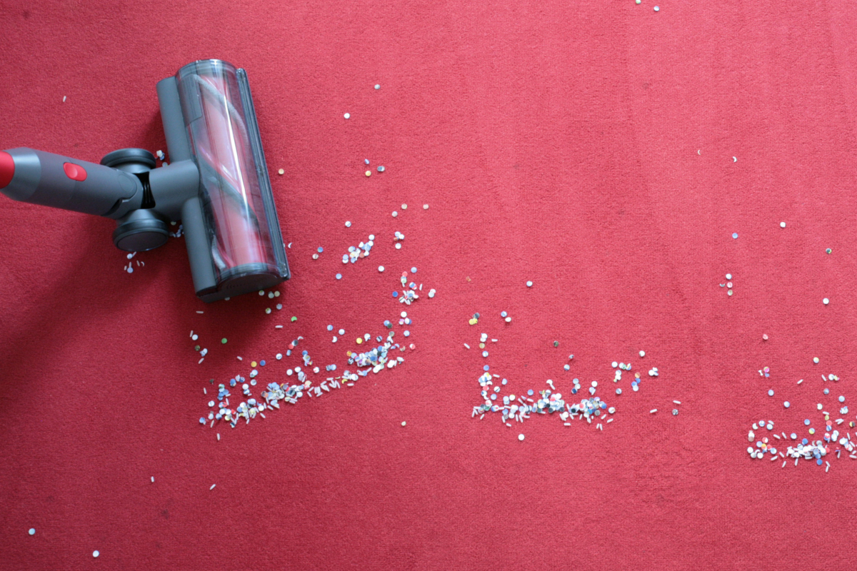 Akkusauger links im Bild saugt Konfetti auf rotem Teppich