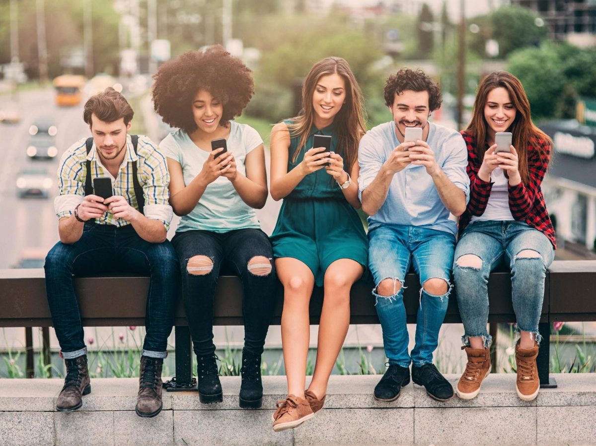 Fünf Leute sitzen auf eine Brücke und benutzen Smartphones.