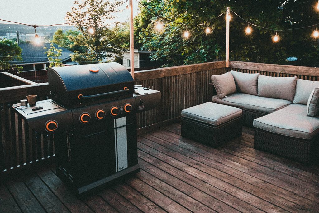 Terrasse mit Holzboden und großem gasgrill mit Sitzgruppe im Hintergrund