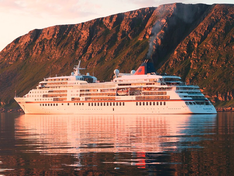 Blick auf Wasser und Kreuzfahrtschiff von der Seite von steiler Küste in orange getauchtem Licht
