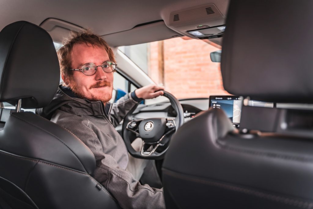 Mann mit Brille sitzt am Steuer und schaut nach hinten gewandt in die Kamera