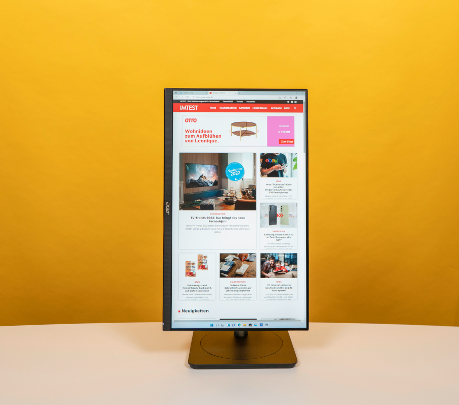 Hochkant gedrehter Monitor mit IMTEST Startseite auf Tisch vor orangenem Hintergrund