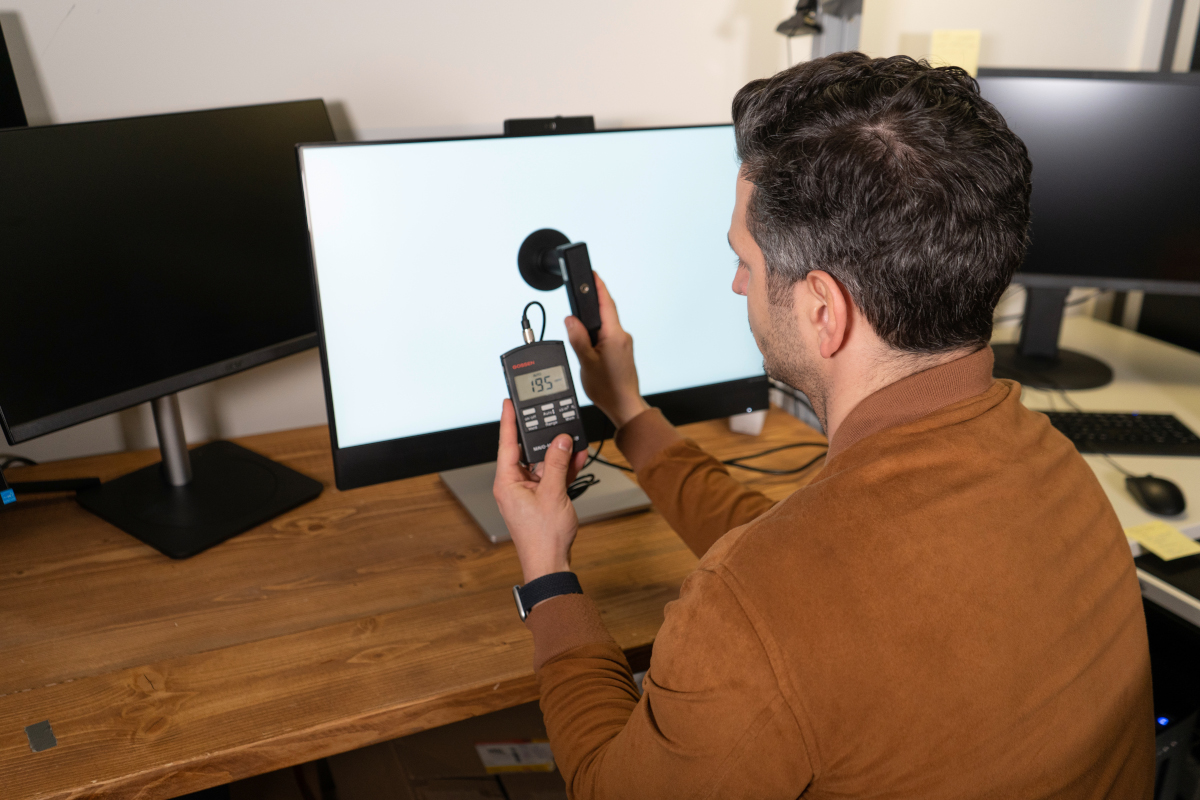 Monitor-Test: Mann mit Messgerät in der Hand vor weißem Monitor