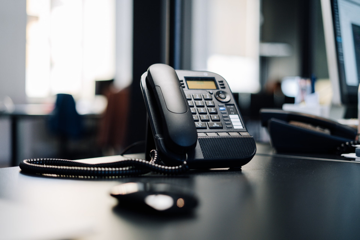 Schwarzes Festnetztelefon auf Bürotisch von Kundenservice, im Hintergrund andere Telefone und Computer