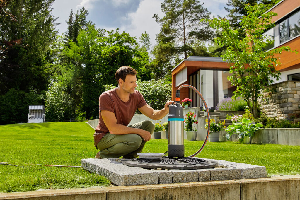 Mann im Garten mit Tauchpumpe vor Brunnen.