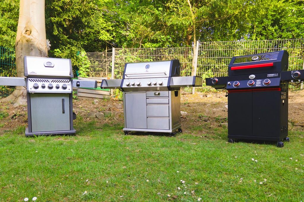 Zwei silberne Gasgrills und ein schwarzer nebeneinander im Garten