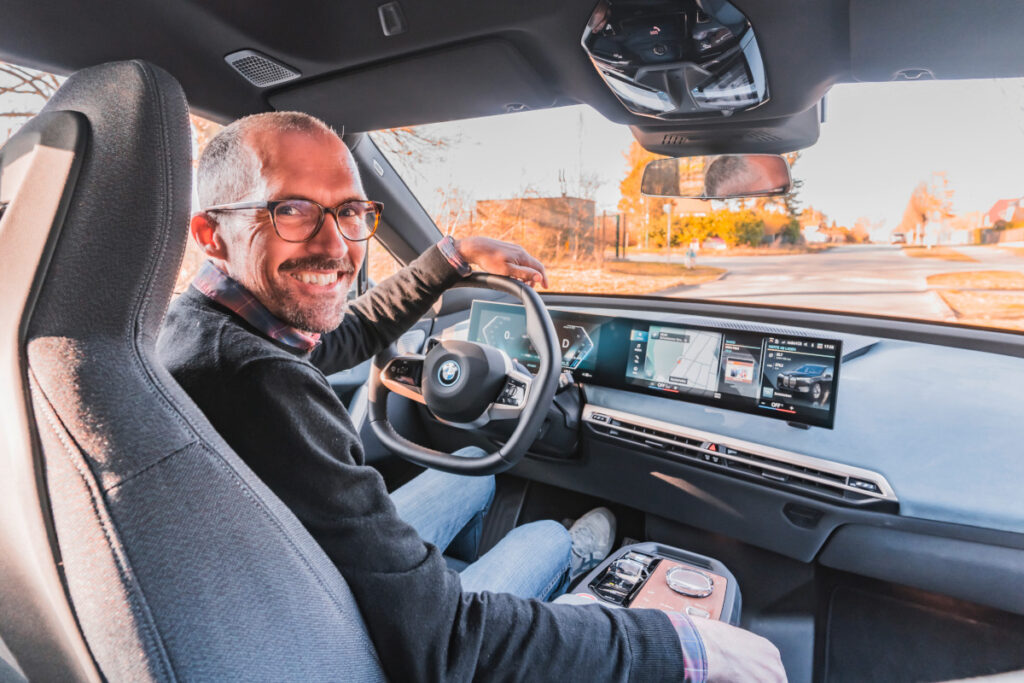 lächelnder Mann am Steuer vom BMW iX schaut über die Schulter in die Kamera