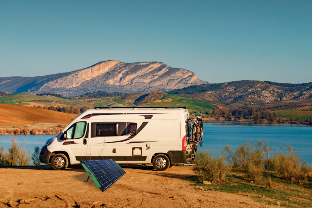 Ein Wohnmobil in der Natur und daneben ein aufgestellter Solarpanel.