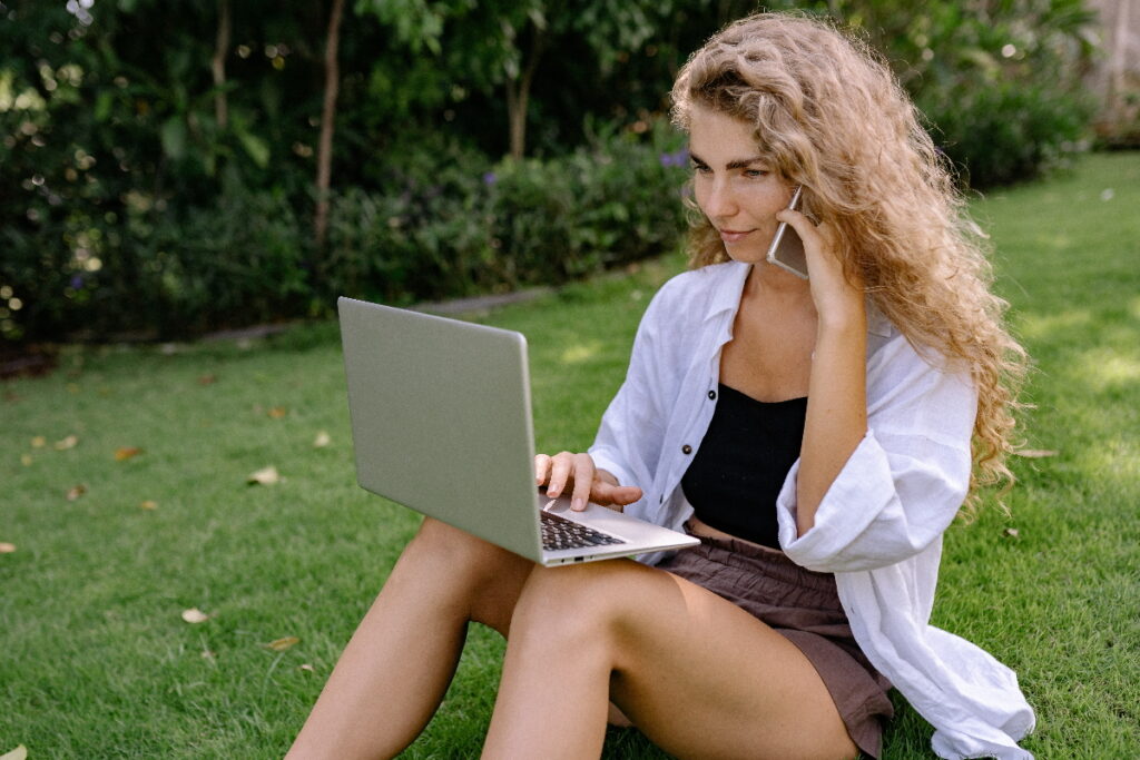 Frau sitzt an Laptop und Handy mit mobilem Internet.