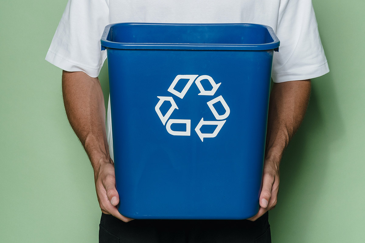 Ein Mann hält einen Eimer mit dem Recycling-Symbol darauf.