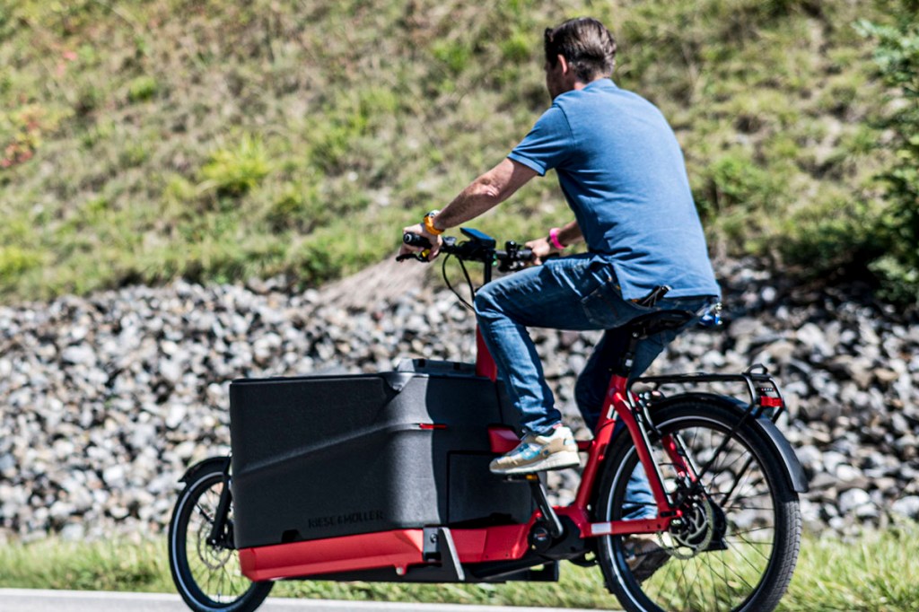 Mann fährt auf Lastenrad auf einer Straße. 