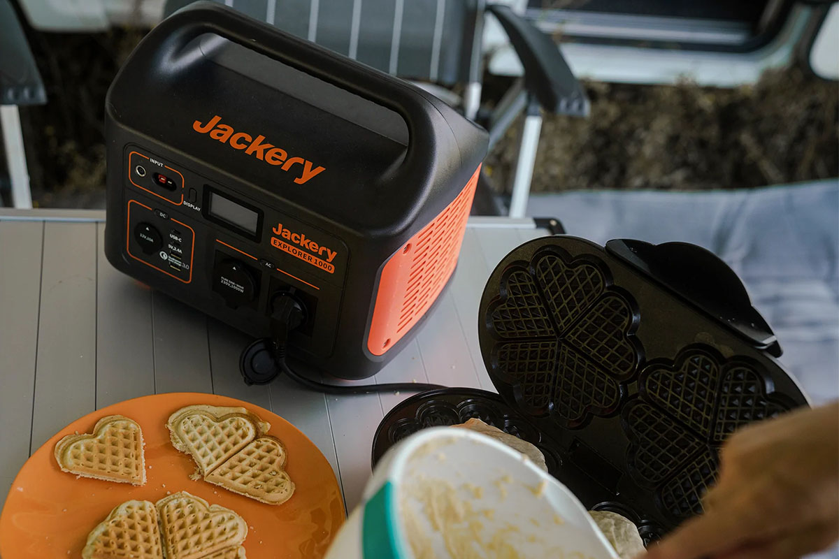 Es ist ein Tisch mit Waffeleisen und Waffel zu sehen. Außerdem die Jackery Explorer 1000 Powerstation als Stromversorgung.