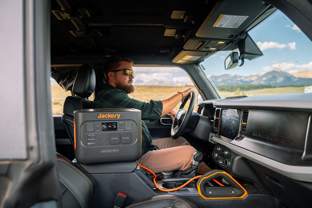 Mann fährt im Auto durch Wüstenlandschaft. Auf dem Beifahrersitz steht ein Jackery Explorer 1000 Pro Solargenerator.