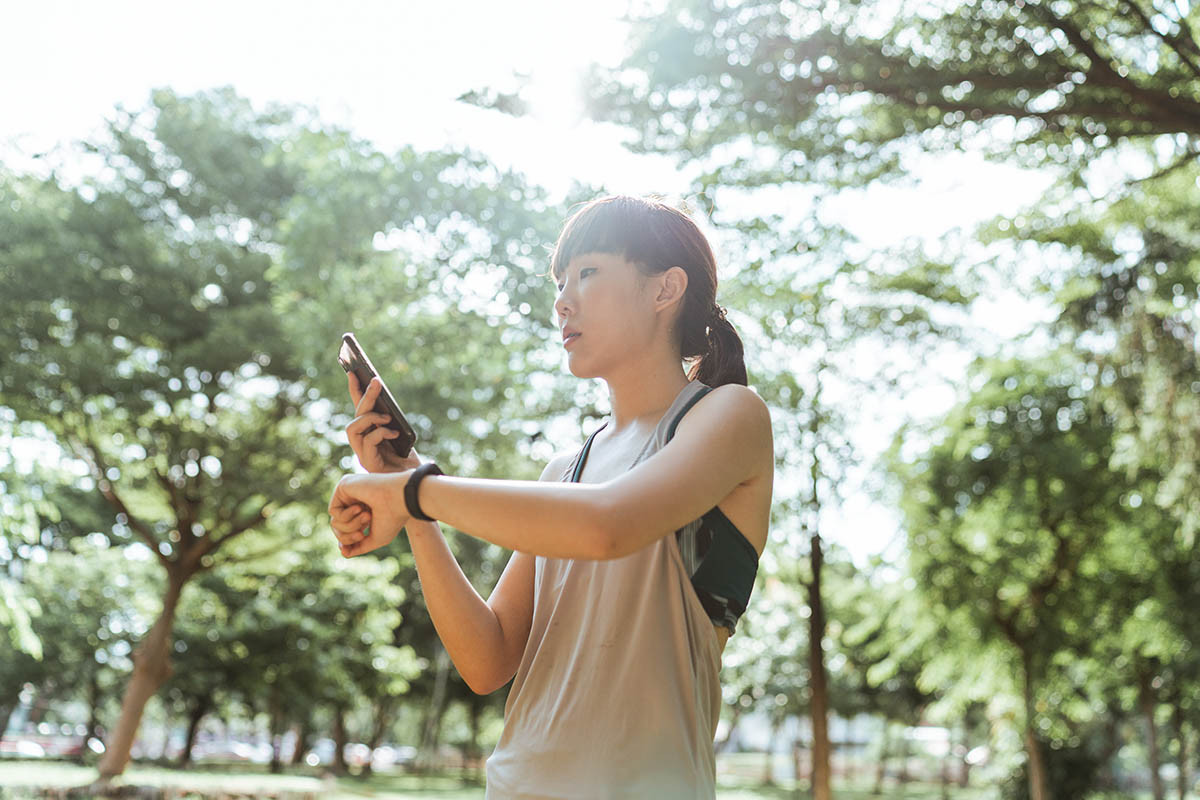 Eine Frau sieht auf ihr Handy sowie ihren Fitnesstracker.