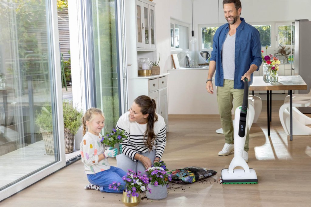 Eine Familie in einem Wohnzimmer mit Saugwischer, Blumen und Blumenerde auf dem Boden.