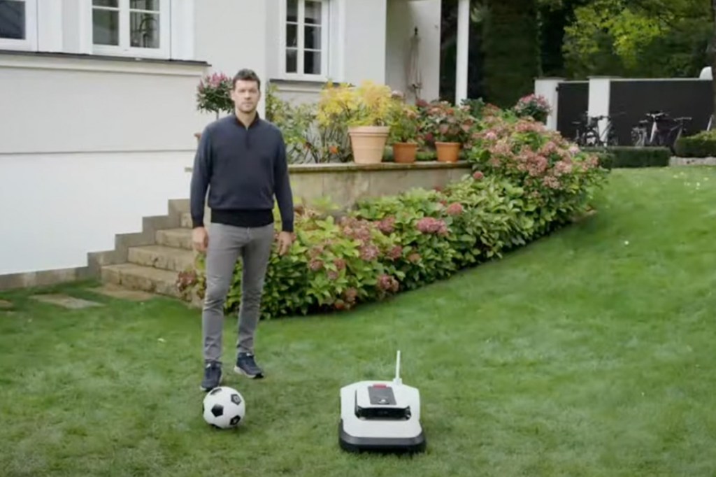 Spokesperson Michael Ballack steht neben dem Ecovacs Mähroboter.