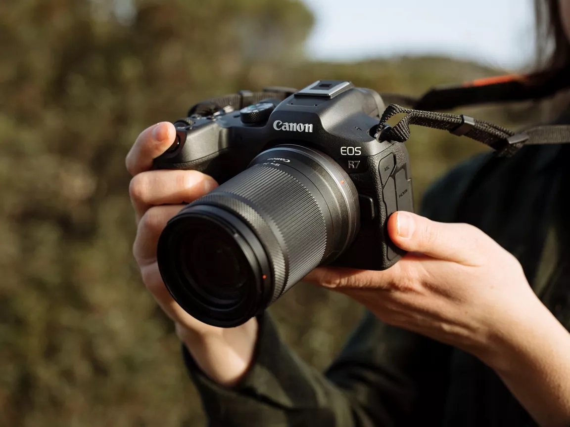 Eine Frau, die die Canon EOS R7 in der Hand hält und auf das Display schaut