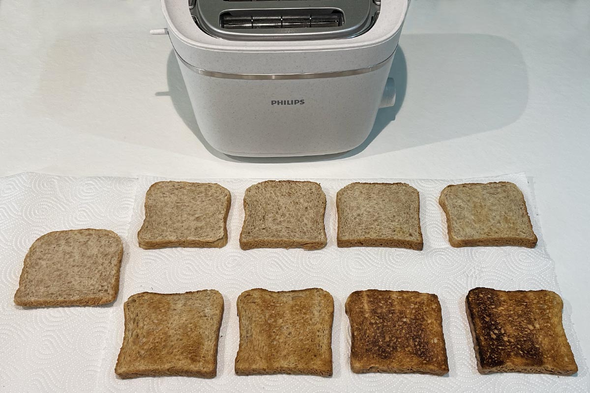 Sieben Toastscheiben unterschiedlich braun, oben im Bild weißer Toaster