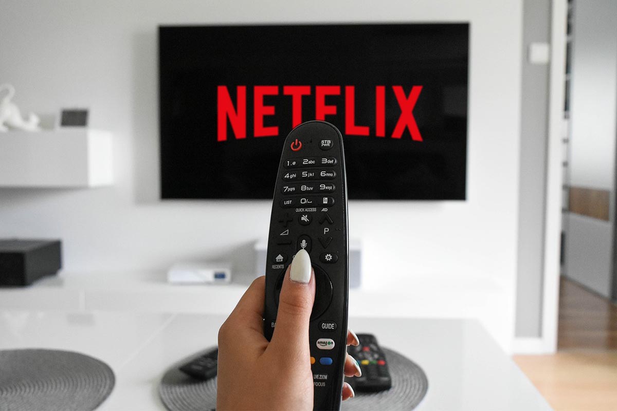 Hand mit Fernbedienung vor Bildschirm mit Logo von Netflix