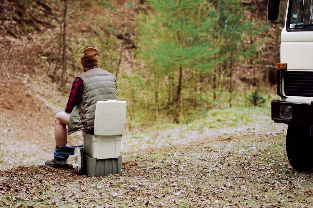 Mann auf der Campingtoilette von Trobolo sitzend, im Wald