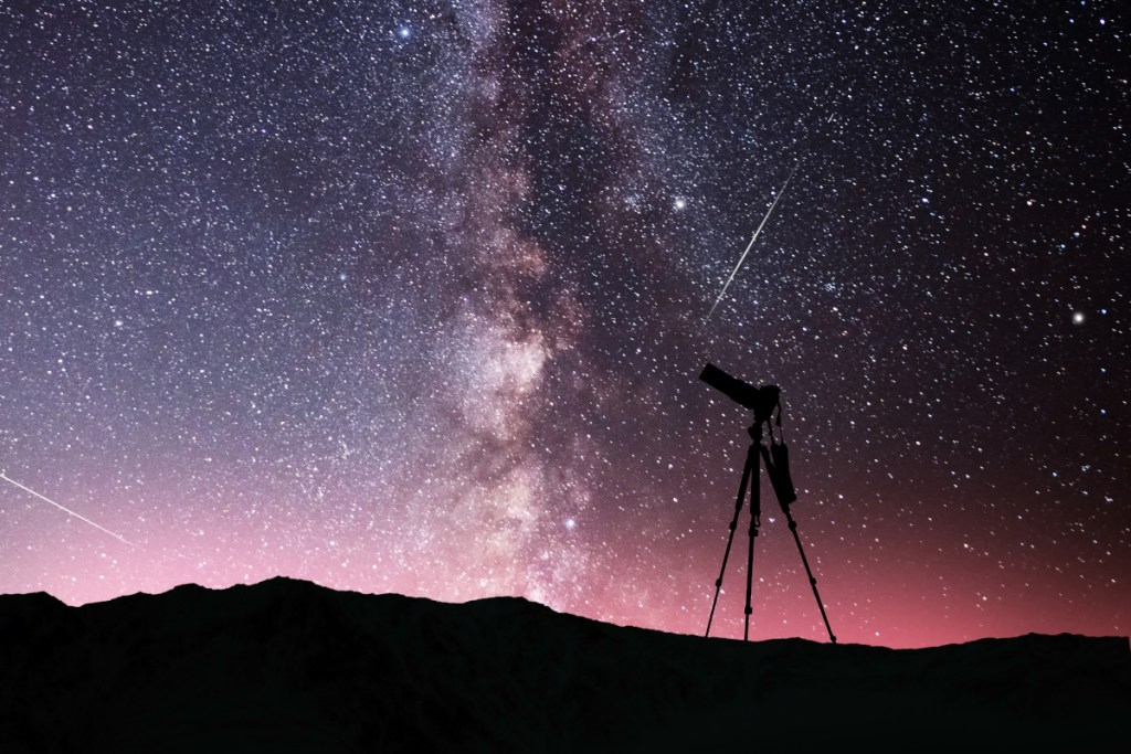 Sternenhimmel in lila mit Kamera auf Stativ als schwarze Silhouette