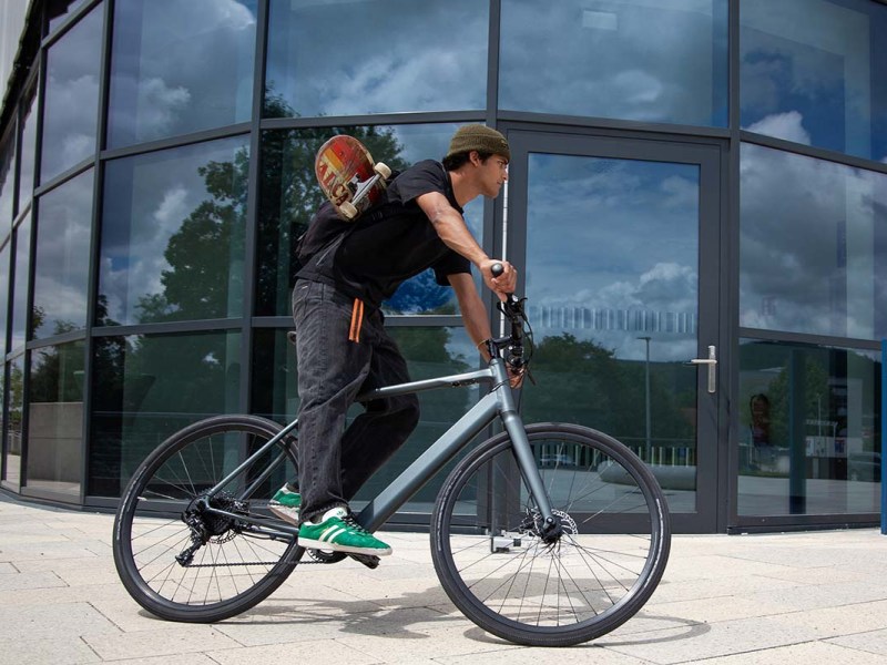 Mann fährt auf dem E-Bike Sydney von coboc an einer gläsernen HÄuserfront vorbei