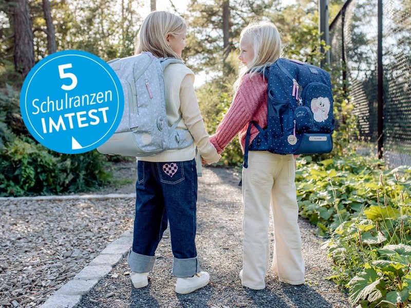 Zwei Kinder mit Schulranzen auf dem Rücken unter freiem Himmel