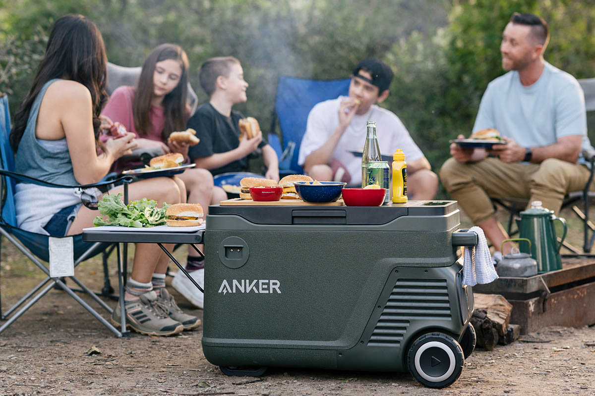 Mehrere Personen an einem Camping-Esstisch im Freien. Im Vordergrund die Anker EverFrost Kühlbox.