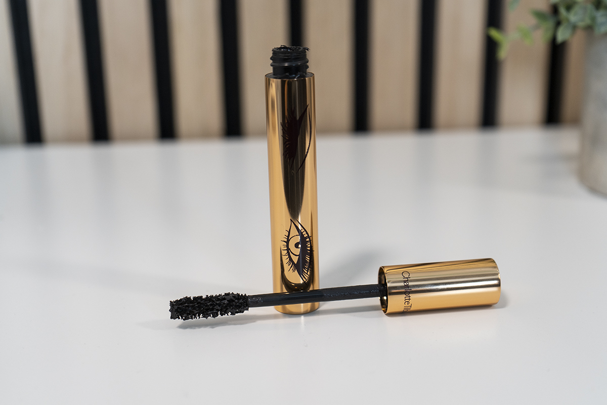 Geöffnete Mascara Flasche mit Bürste vorne auf weißem Tisch liegend, golden