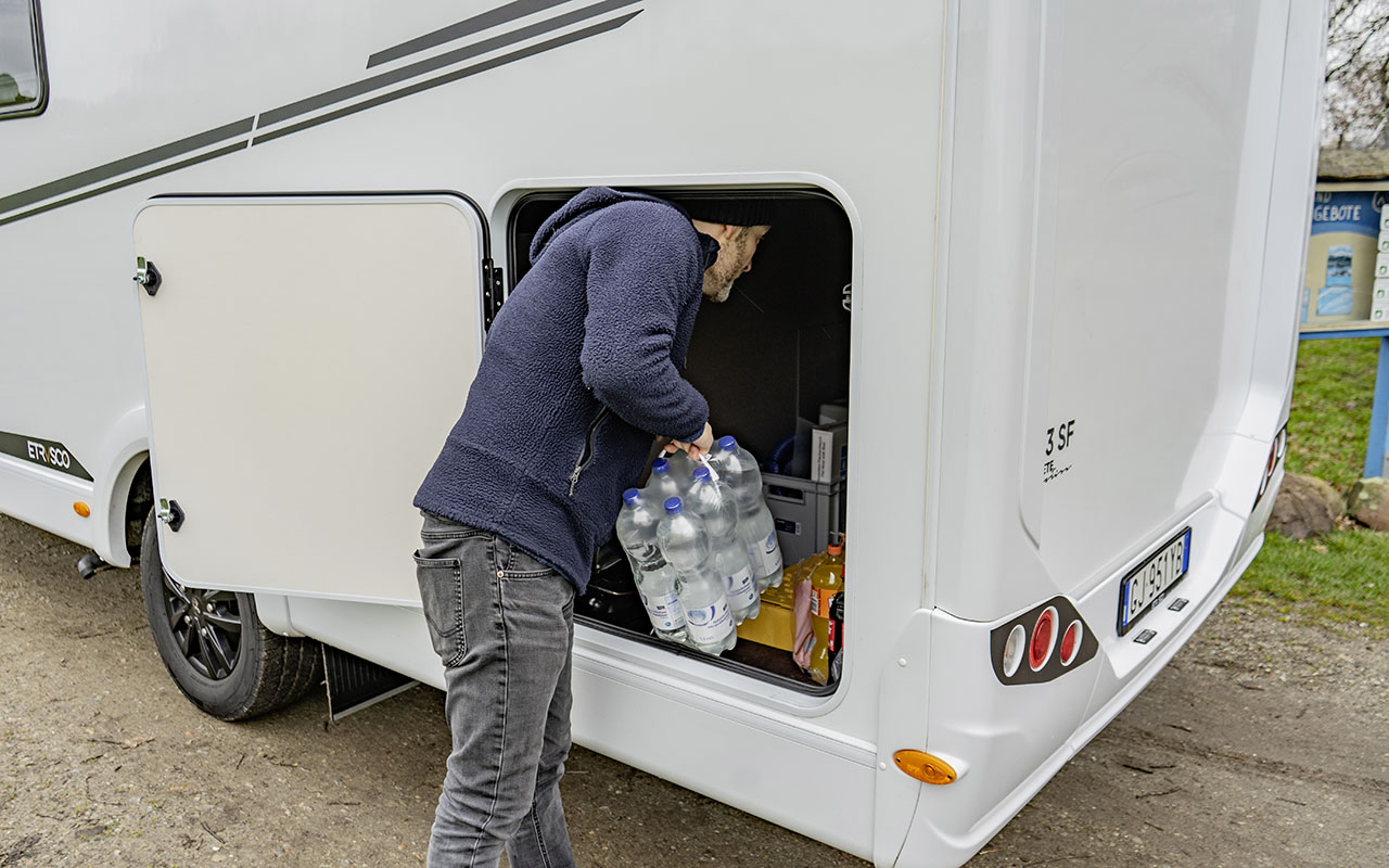 Mann hebt Getränke in die Heckgarage des teilintegrierten Wohnmobils Etrusco T 7.3 SF.