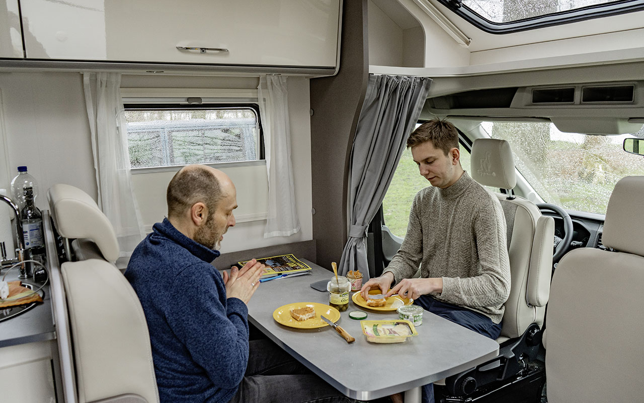 Zwei Männer sitzen und essen im Wohnbereich des teilintegrierten Wohnmobils Etrusco T 7.3 SF.