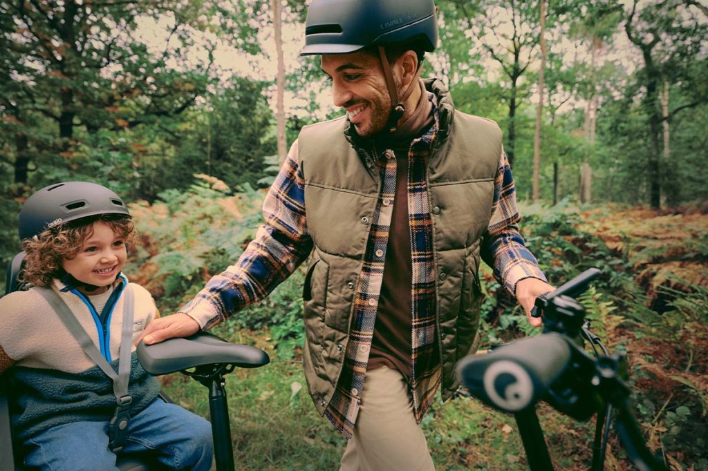 Mann steht hinter seinem E-bike und lacht seinem Kind zu, welches hinten auf dem Kindersitz sitzt