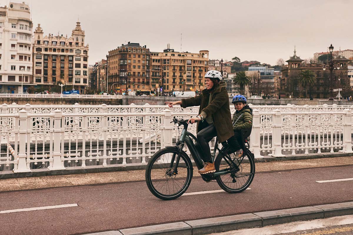 Frau fährt mit Kiind im Kindersitz dem fahrrad durch eine Stadt.