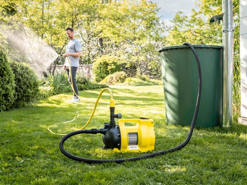 Ein Mann bewässert seinen Garten, daneben eine Wasserpumpe.