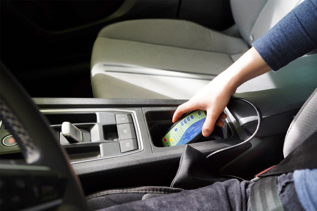 Eine Frau sitzt im Auto und greift nach einer Fernbedienung.