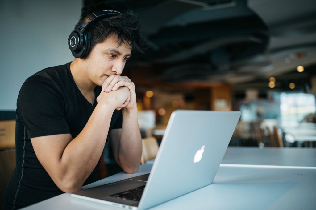 Ein Mann sitzt vor einem Laptop mit einem erstaunten Gesichtsausdruck.