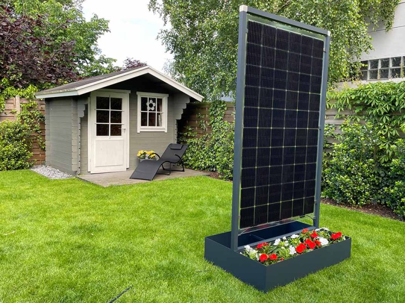 Der neue Solar-Blumenkübel von GreenAkku in einem Garten mit Gartenhäuschen im Hintergrund.