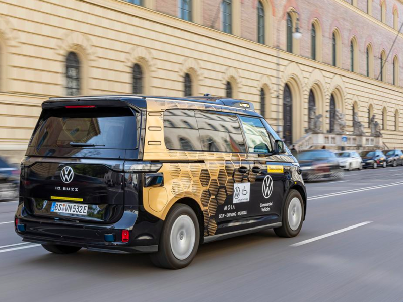 Der Mini-Van ID.Buzz während der Fahrt von schräg hinten rechts fotografiert, im Hintergrund ein historisches Gebäude