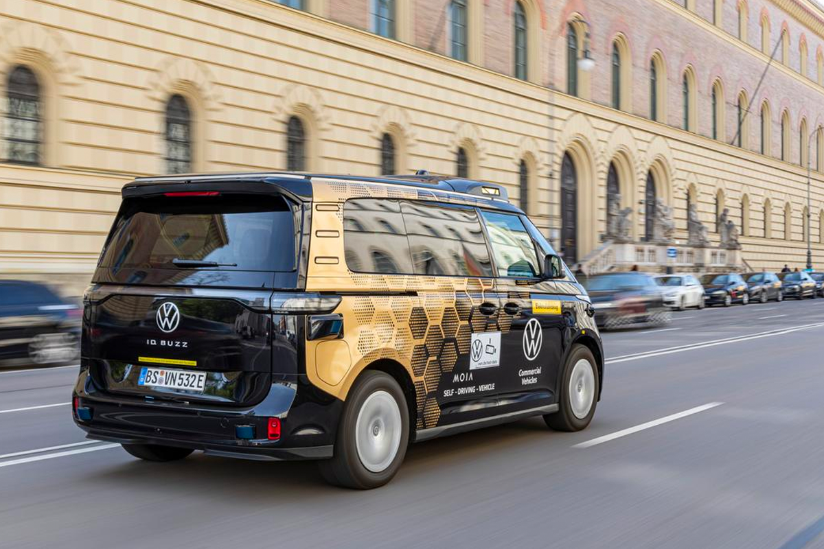 Der Mini-Van ID.Buzz während der Fahrt von schräg hinten rechts fotografiert, im Hintergrund ein historisches Gebäude