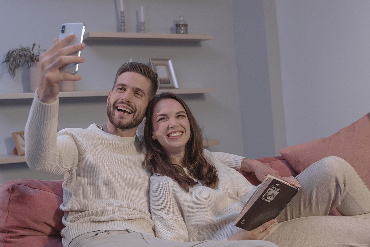 Ein Pärchen sitzt mit Handy auf dem Sofa.