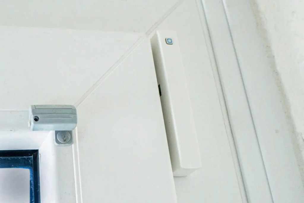 Ecke eines Fensters mit weißem Rahmen an dem ein Rechteckiger Sensor ist