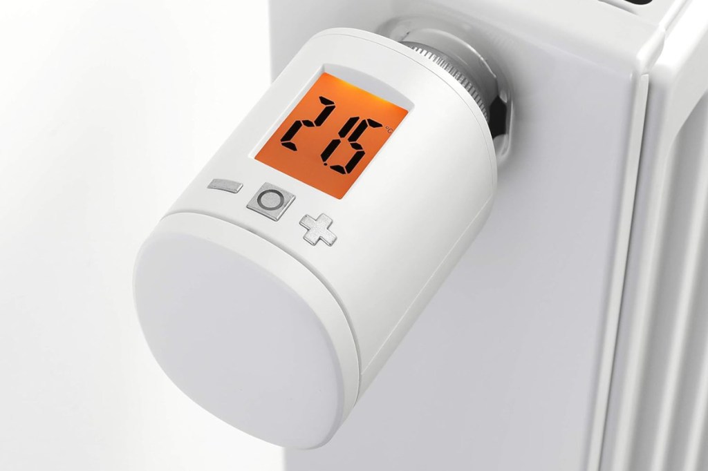 Weißes rundes Heizkörperthermostat von Homepilot mit orange leuchtendem Display, das 21,5 Grad anzeigt schräg von oben an weißem Heizkörper vor weißem Hintergrund