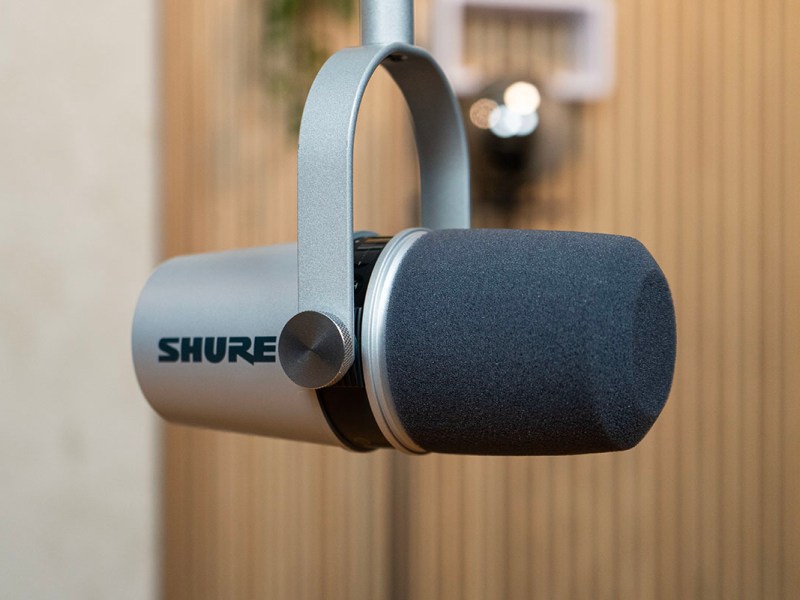 Das silberne Mikrofon Shure MV7 hängend vor einer Holzwand