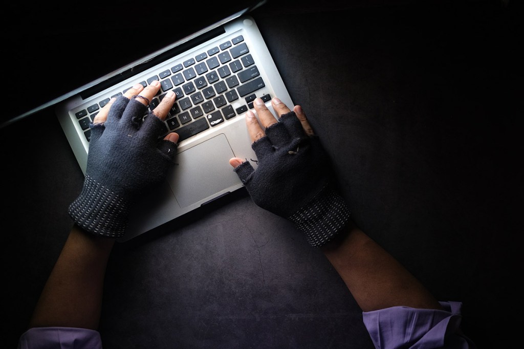 Hände in Handschuhen tippen auf einer Tastatur.