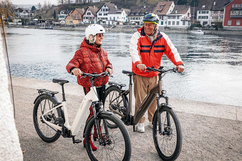 Zwei Personen stehen neben ihren E-Bikes, dahinter ein Fluss