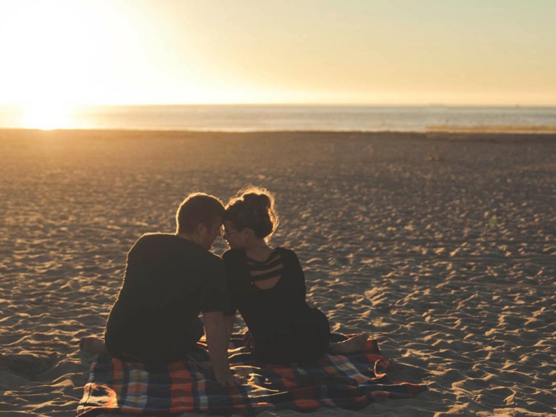 Zwei Menschen sitzen bei Sonnenaufgang am Strand