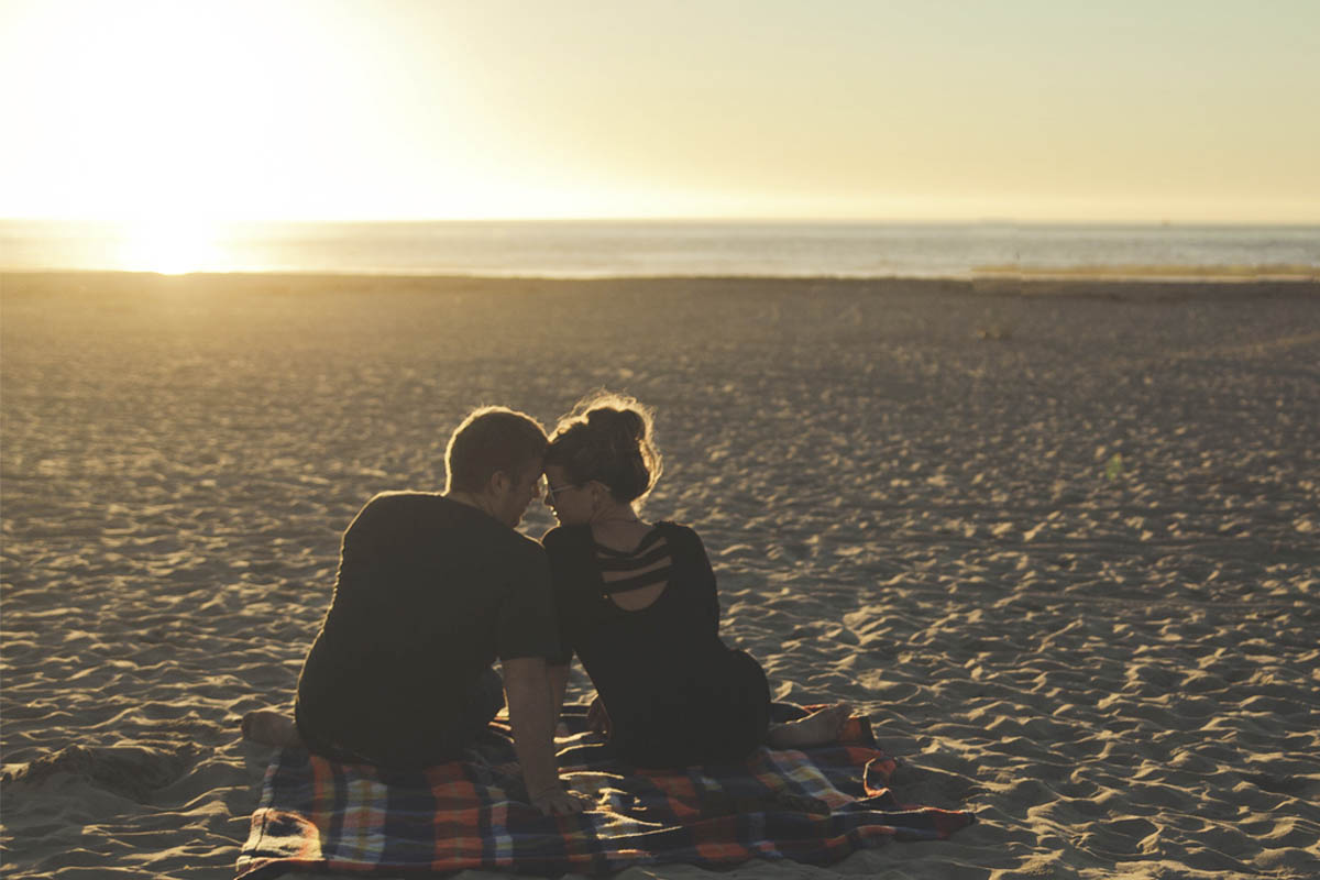 Zwei Menschen sitzen bei Sonnenaufgang am Strand