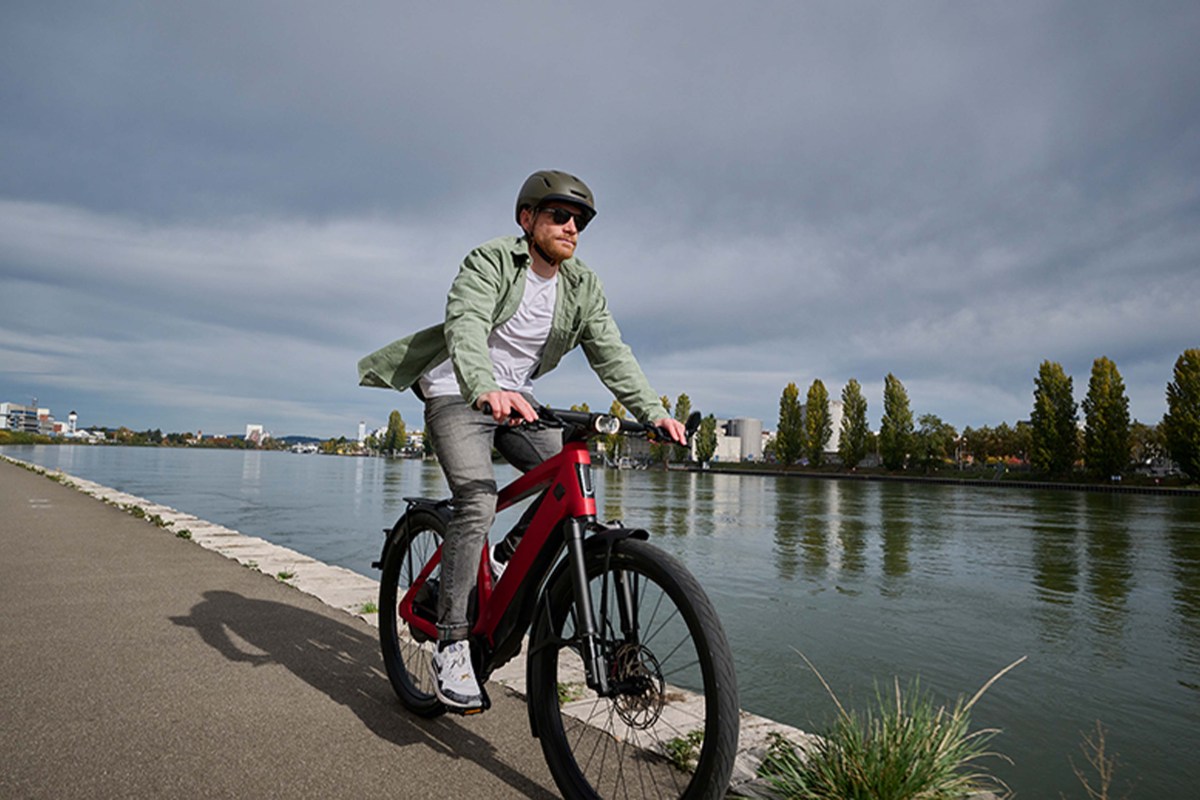 Mann fährt mit einem roten E-Bike einen Weg an einem Fluss entlang